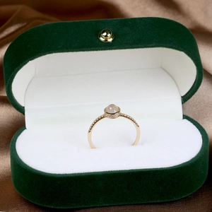 Close-up of gold ring with round white gemstone in a green velvet jewelry box