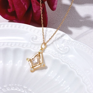 Golden kite pendant necklace with clear crystal and opal accents on a vintage dish