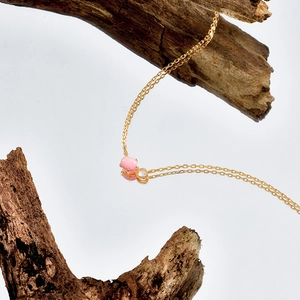 Elegante collana in argento dorato con pietra rosa ovale e zircone bianco su superficie specchio