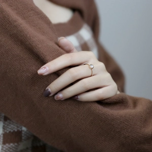 Detail of rose gold ring with moonstone and pavé diamonds worn on hand with knit background