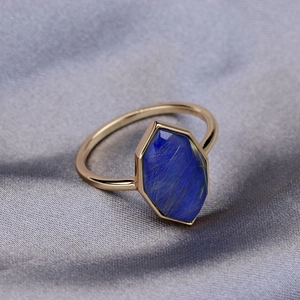 Detail shot of a hexagonal blue lapis lazuli stone set on a golden ring over grey silk
