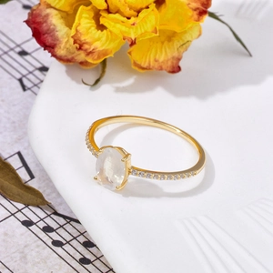Artistic detail of gold-plated silver ring with oval moonstone on white porcelain plate