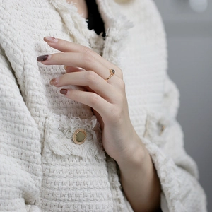 Nahaufnahme eines schmalen Goldrings mit dunklem Edelstein an einem Model in Tweedjacke