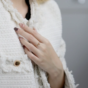 Nahaufnahme des minimalistischen Goldrings mit rundem Edelstein auf weißem Tweed-Stoff