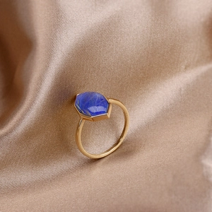 Macro shot of hexagonal blue gemstone ring with gold band on champagne silk fabric