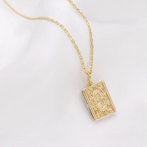 Close-up of gold locket necklace with vintage floral relief on elegant white fabric