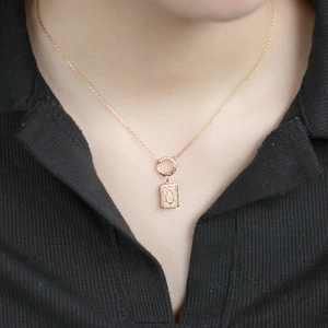 Close-up of vintage style gold-plated necklace with embossed rectangular book pendant