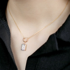Detail of a vintage-style gold book pendant with multi-color gemstones on a neck chain