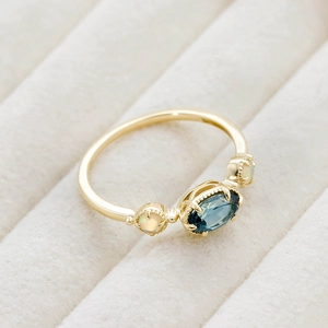 Macro d'une bague dorée avec topaze bleue de Londres et opale sur velours beige
