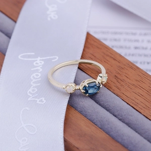 Vue détaillée de la bague en topaze bleue et opale posée sur un ruban violet Forever Love