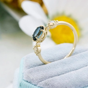 Macro d'une bague dorée avec topaze bleue ovale et opales dans un écrin à bijoux