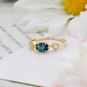 Gros plan d'une bague en or avec topaze bleue de Londres et opales sur marguerites