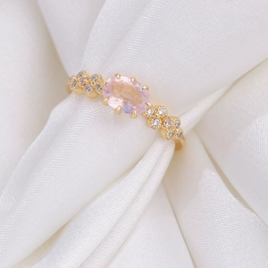 Macro view of gold S925 silver ring with oval pink quartz and zircon accents on white silk