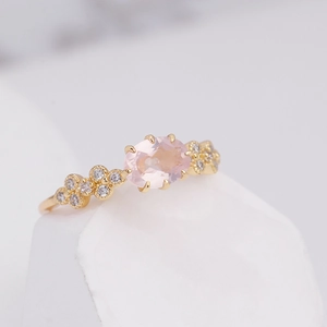 Detailed shot of oval pink crystal gemstone in rose gold setting with zircon accents