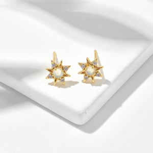 Detailaufnahme goldener Sternen-Ohrstecker mit Opal auf einem weißen Steinsockel platziert