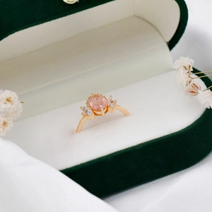 Macro shot of oval pink strawberry quartz ring with zircon accents in green velvet box