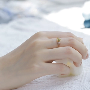 Detailed view of a gold flower ring with green peridot and pink stones on a lace background