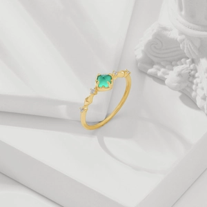 Gros plan d'une bague dorée S925 avec émeraude pain de sucre et diamants scintillants