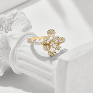 Dettaglio ravvicinato di un anello a fiore dorato con zirconi su colonna bianca