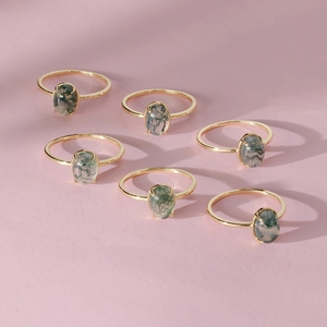 Top view of six gold rings with moss agate gemstones on a soft pink background