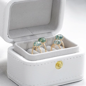 Detail of two gold moss agate rings with four-prong settings in a white leather jewelry box