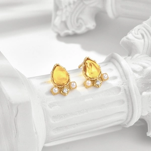 Makroaufnahme von goldenen Bernsteinohrringen mit Wassertropfen und weißen Perlen
