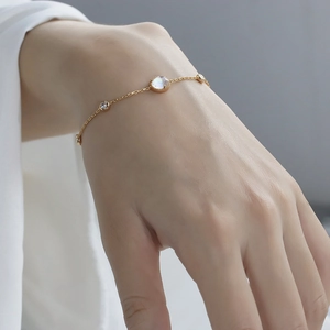 Classic gold bracelet with white crystal and bubble shell charm on a woman's wrist