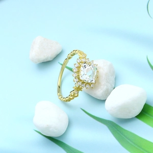 Detail van vergulde S925 zilveren ring met heldere topaas en diamantkrans op witte kiezelstenen