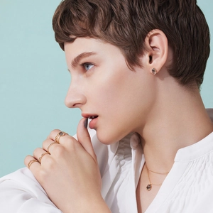 Detalle de collar dorado y anillos superpuestos con piedras oscuras en modelo femenina