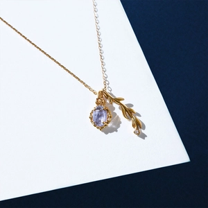 Close-up of golden branch pendant and purple gemstone on a delicate silver necklace