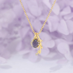 Elegant gold pendant necklace with purple gemstone and leaf detail on floral background