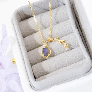 Elegant gold necklace with oval purple gemstone and leaf detail in a jewelry box