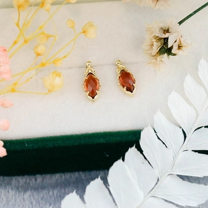 Primer plano de aretes de granate en montura dorada dentro de una caja de regalo con flores