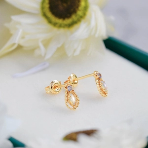 Detailed close-up of vintage gold teardrop earrings with opal stone and purple crystal