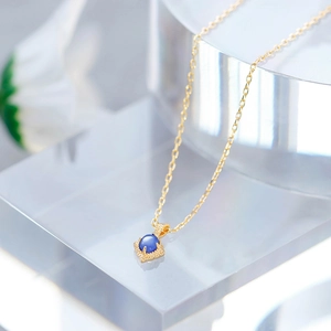 Detailed close-up of a vintage-style gold square pendant with a round blue gemstone inlay