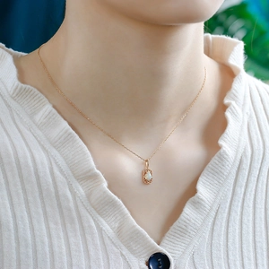 Close-up of a teardrop opal pendant on a gold chain worn over a white knit sweater