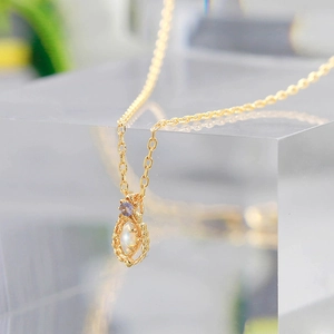 Macro detail of 14K gold-plated necklace featuring opal pendant and purple gemstone