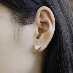 Close-up of 14K gold plated heart stud earrings with pink shell and white zircon on ear