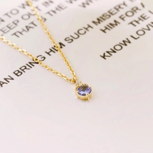 Détail d'un pendentif en pierre violette ronde sur une fine chaîne dorée en argent S925