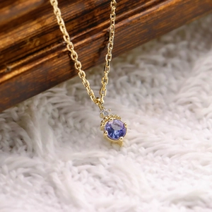 Détail macro du pendentif en or avec tanzanite violette ronde et diamant blanc sur chaîne O