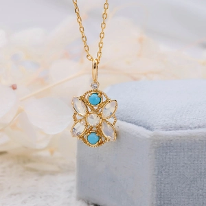 Primer plano macro de colgante floral en oro de 18K con ópalo y turquesa en joyero