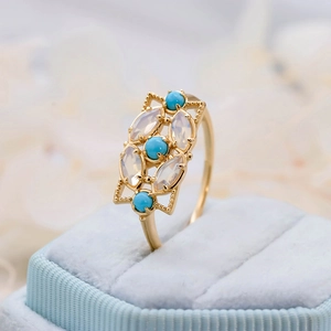 Détail d'une bague vintage dorée avec turquoise et opale dans un écrin en velours