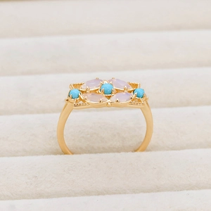 Détail d'une bague vintage dorée avec pierres lavande et turquoise sur boîte beige