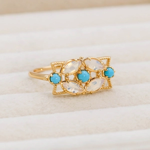 Détail de la bague vintage dorée avec turquoise et opale sur velours beige