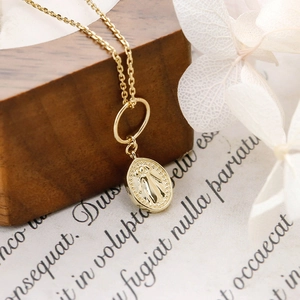 Macro detail of 14K gold plated S925 silver Miraculous Medal pendant on a wooden surface