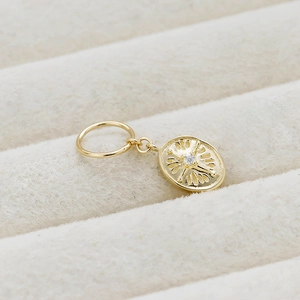 Macro detail of oval gold coin pendant featuring radial patterns and a central zircon stone