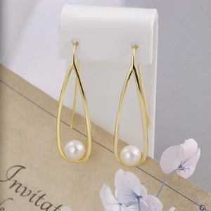 Detail of drop-shaped gold earrings with white freshwater pearls on a white display stand