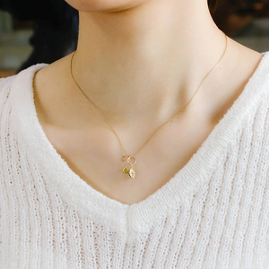 Double pendant gold necklace with green gemstone and textured oval charm on white sweater