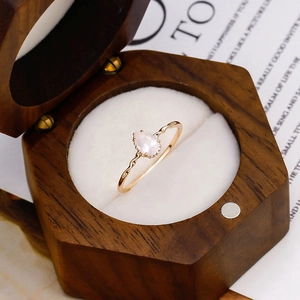 Detail eines tropfenförmigen Rosenquarz-Rings in 14K Gold auf einer sechseckigen Holzkiste