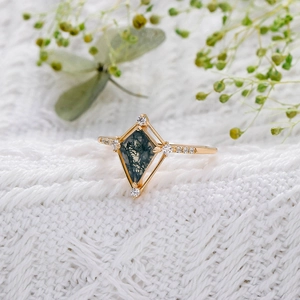 Gros plan d'une bague en agate mousse taille cerf-volant sur tissu blanc texturé